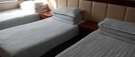 A hotel room with two single beds, a wooden headboard, and a window providing natural light.