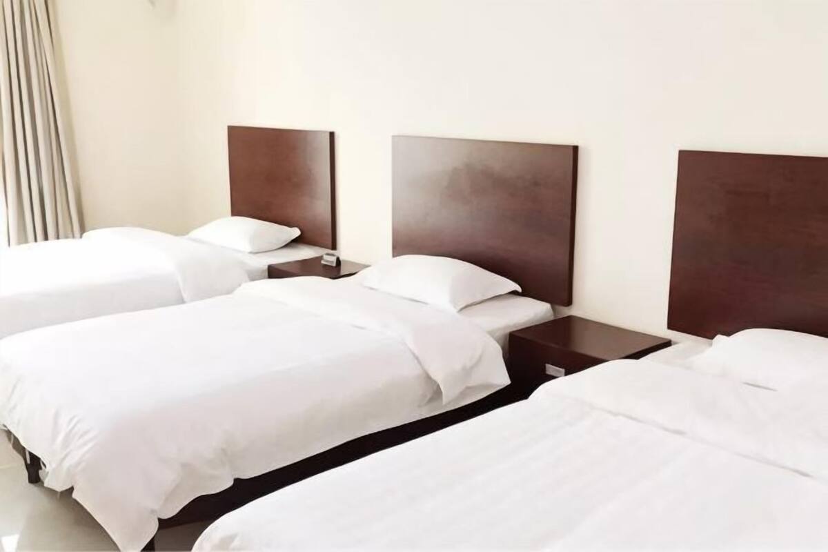 Ein Hotelzimmer mit drei Einzelbetten, jeweils mit einem Holz-Kopfteil und weißer Bettwäsche.