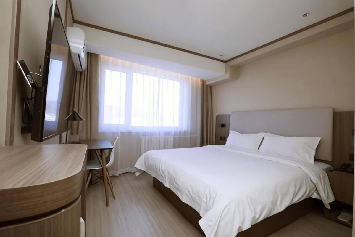 Ein Hotelzimmer mit Bett, Schreibtisch, Stuhl, Fernseher und einem Fenster mit Vorhängen.