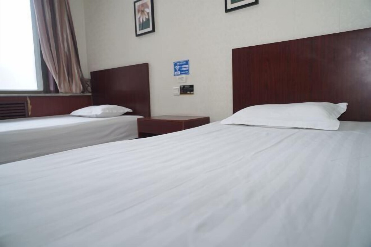 A hotel room with two single beds, a wooden headboard, a nightstand, and a window with curtains.
