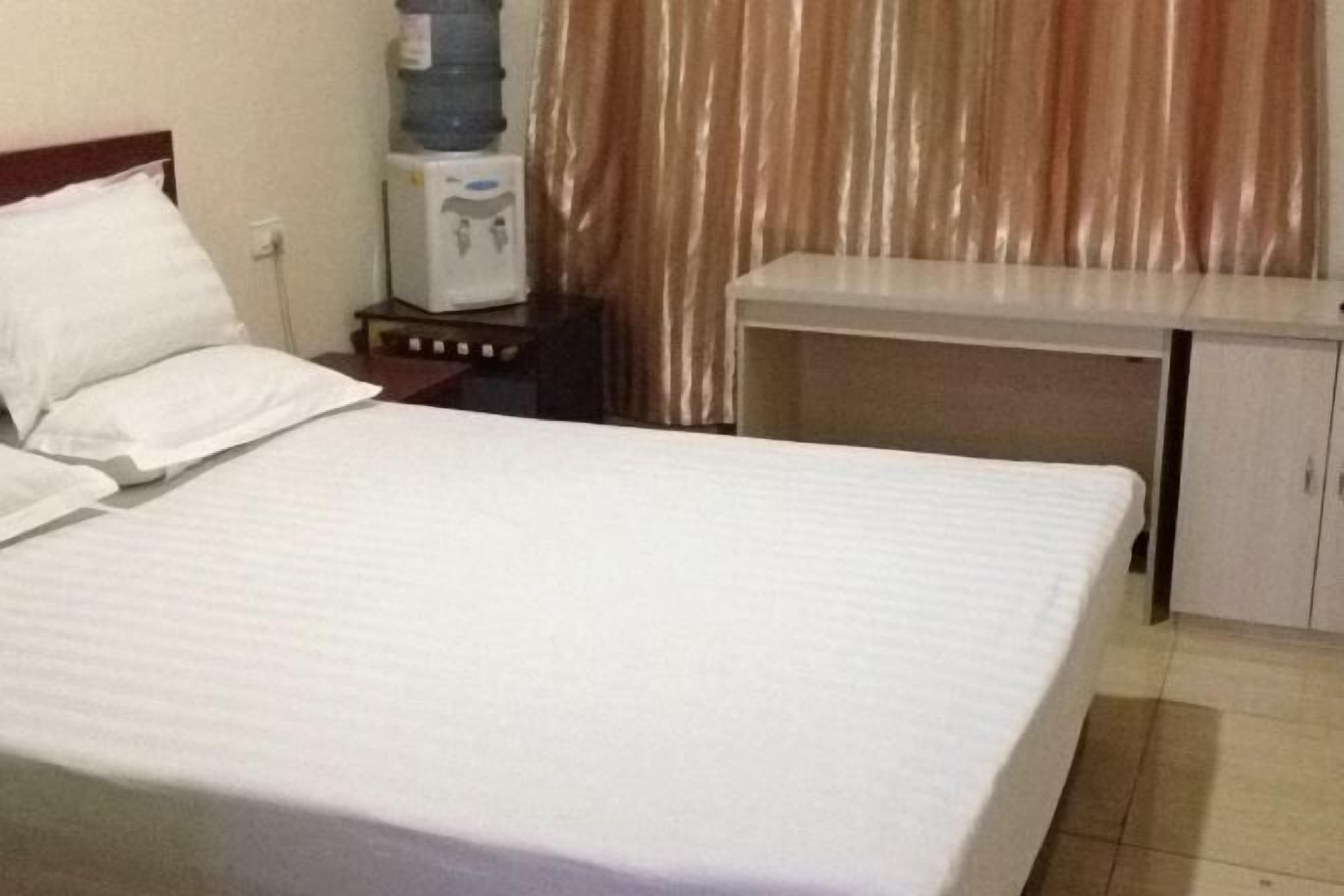 Ein Hotelzimmer mit Bett, Schreibtisch, Wasserspender und Vorhang.