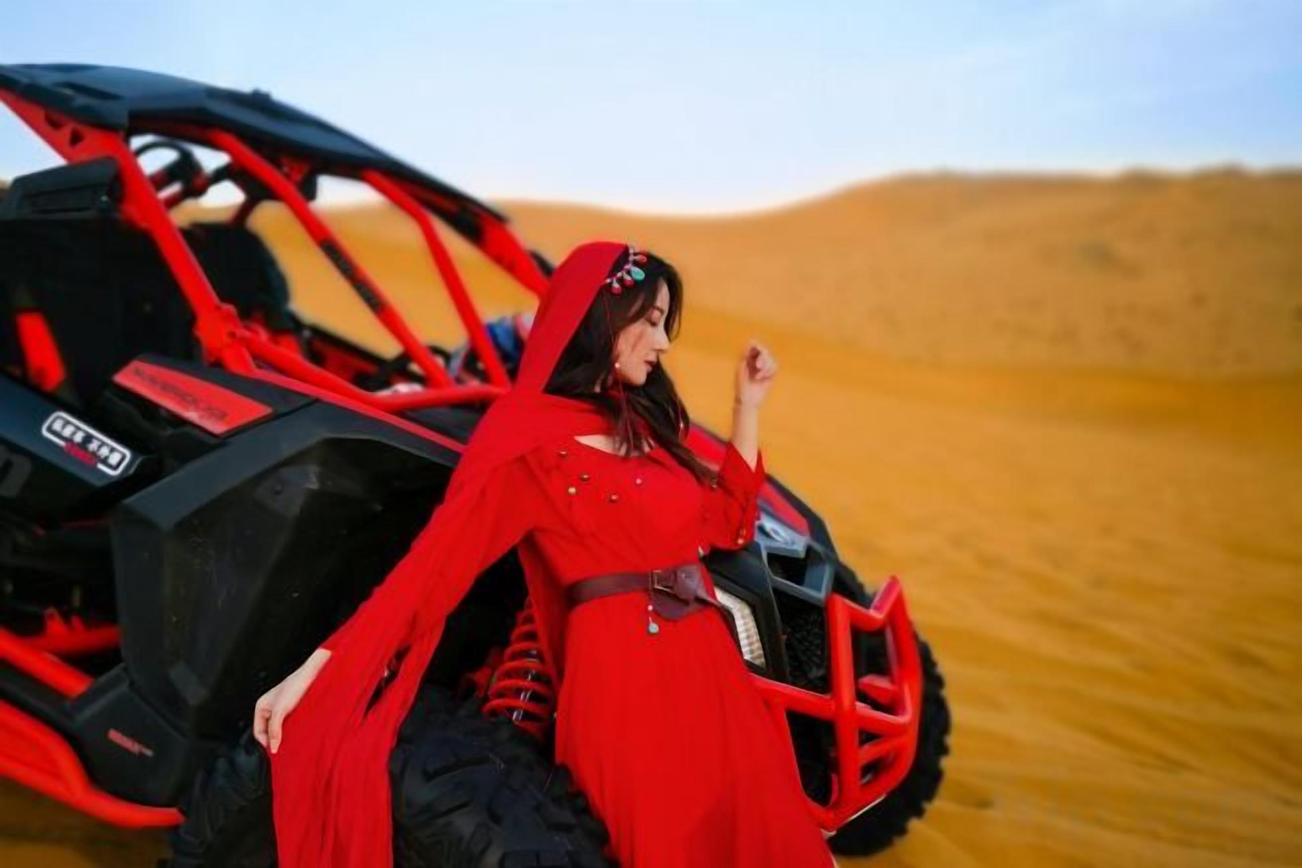 Una persona vestida de rojo sentada en un vehículo todoterreno rojo en un paisaje desértico.