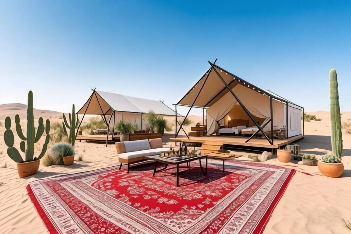 A desert tented accommodation with a red patterned rug, seating area, and cacti.