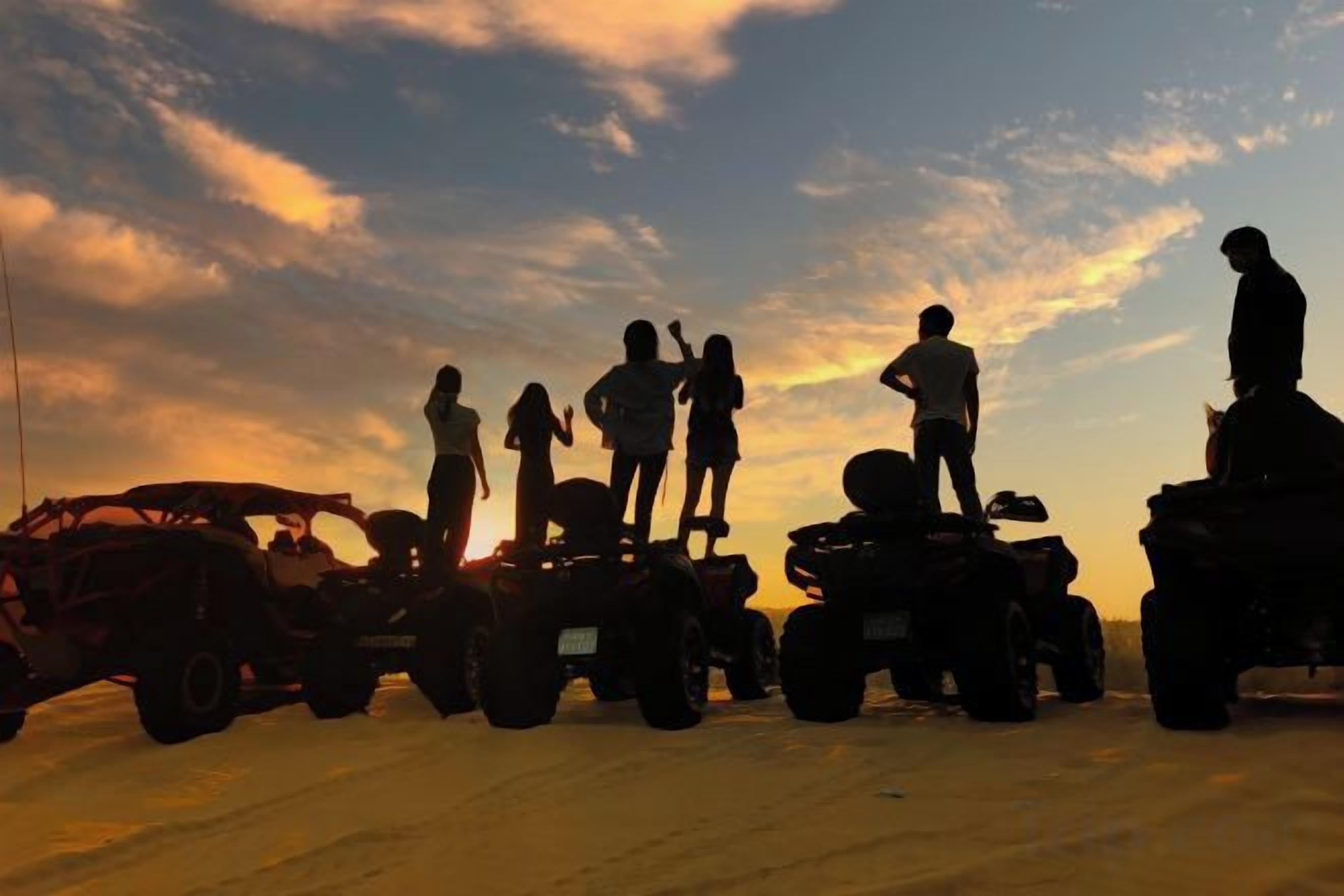 Eine Gruppe von Menschen fährt bei Sonnenuntergang mit Quads.