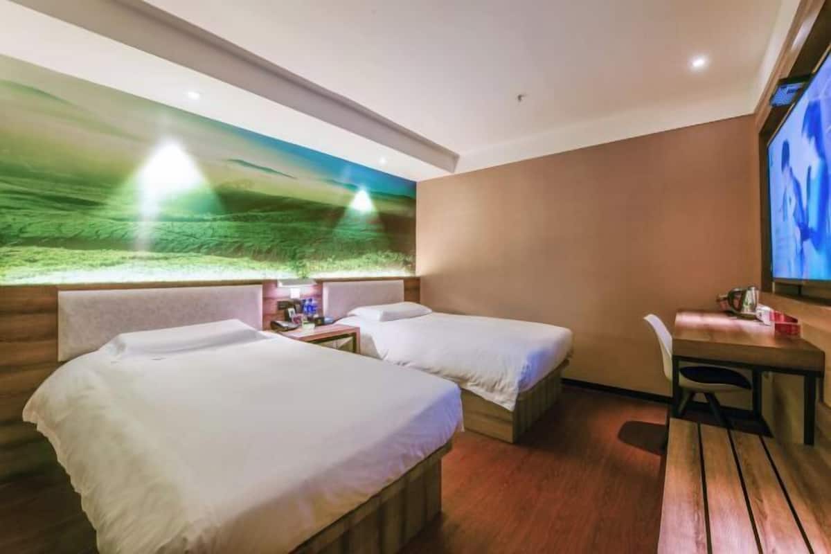 Ein Hotelzimmer mit zwei Betten, einem Schreibtisch, einem Stuhl und einem großen Fernsehbildschirm.
