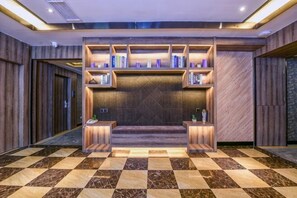 Um lobby com piso xadrez, área de estar central com estantes de livros e parede de madeira.