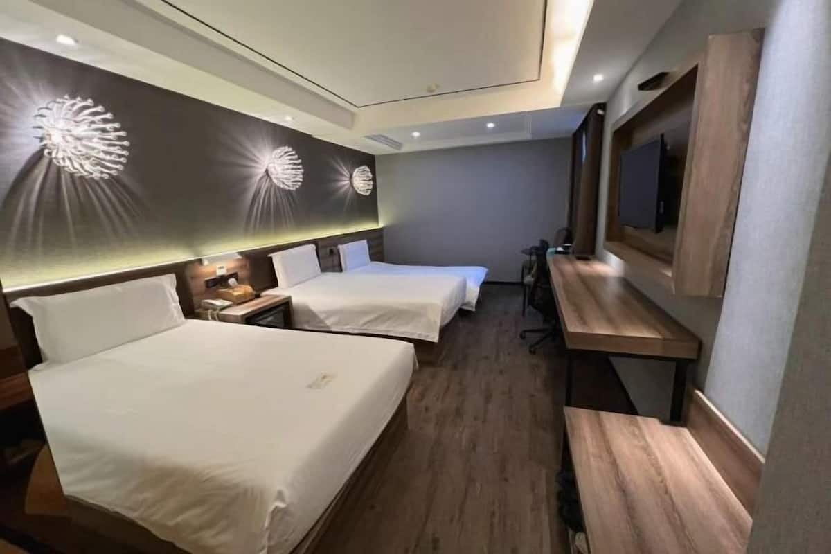 Ein Hotelzimmer mit zwei Betten, einem Schreibtisch, einem Stuhl und einem an der Wand befestigten Fernseher.
