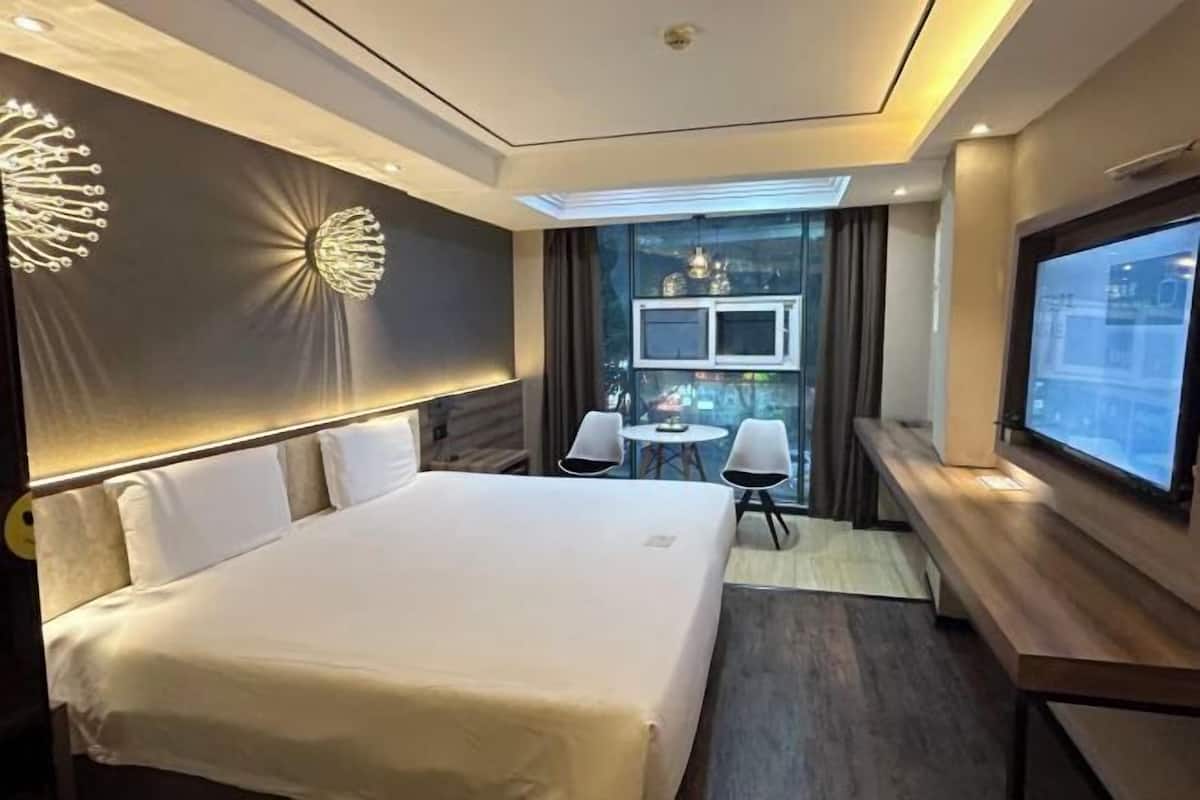 Ein Hotelzimmer mit Bett, Fernseher, Schreibtisch und einer kleinen Sitzecke.