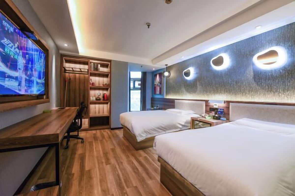 Ein Hotelzimmer mit zwei Betten, einem Schreibtisch, einem Fernseher und einem Bücherregal.