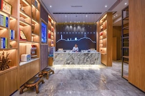 Zona de recepción de un hotel con mostrador de mármol, estanterías de madera y una persona de pie tras el mostrador.