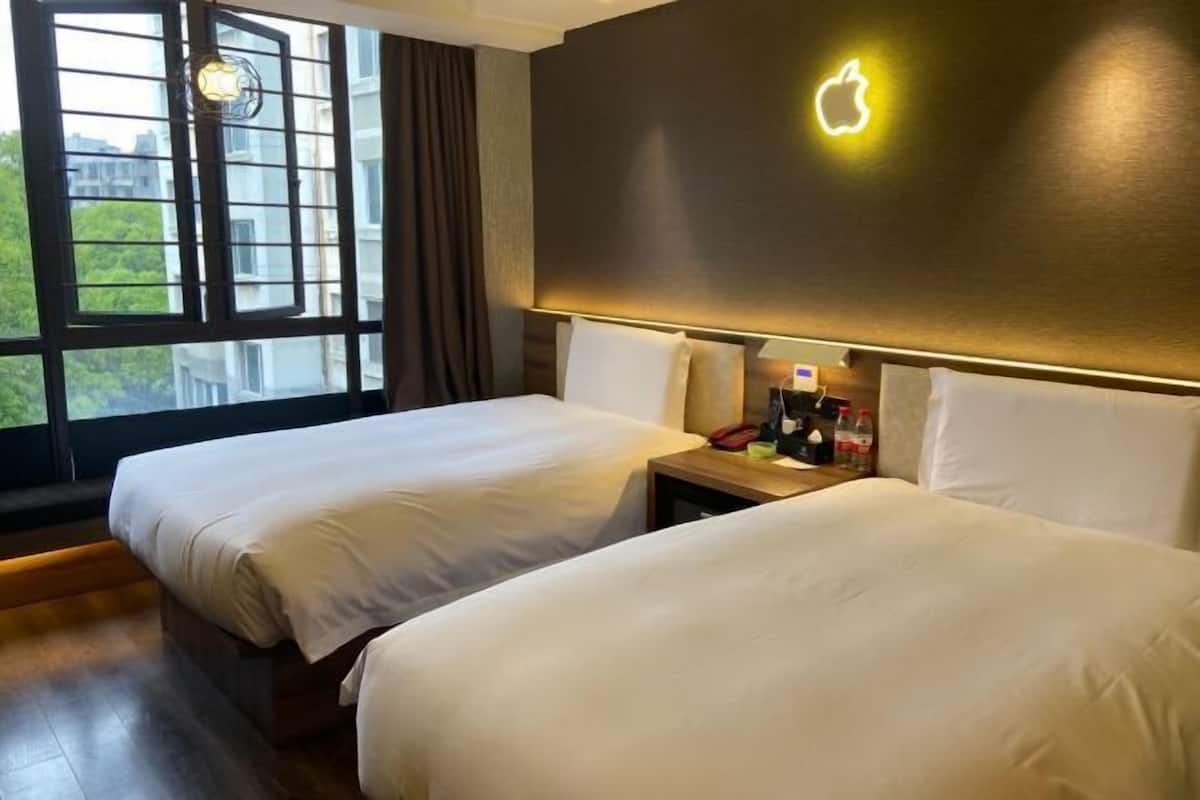 Ein Hotelzimmer mit zwei Betten, einem Nachttisch mit Lampe und dem Apple-Logo an der Wand.