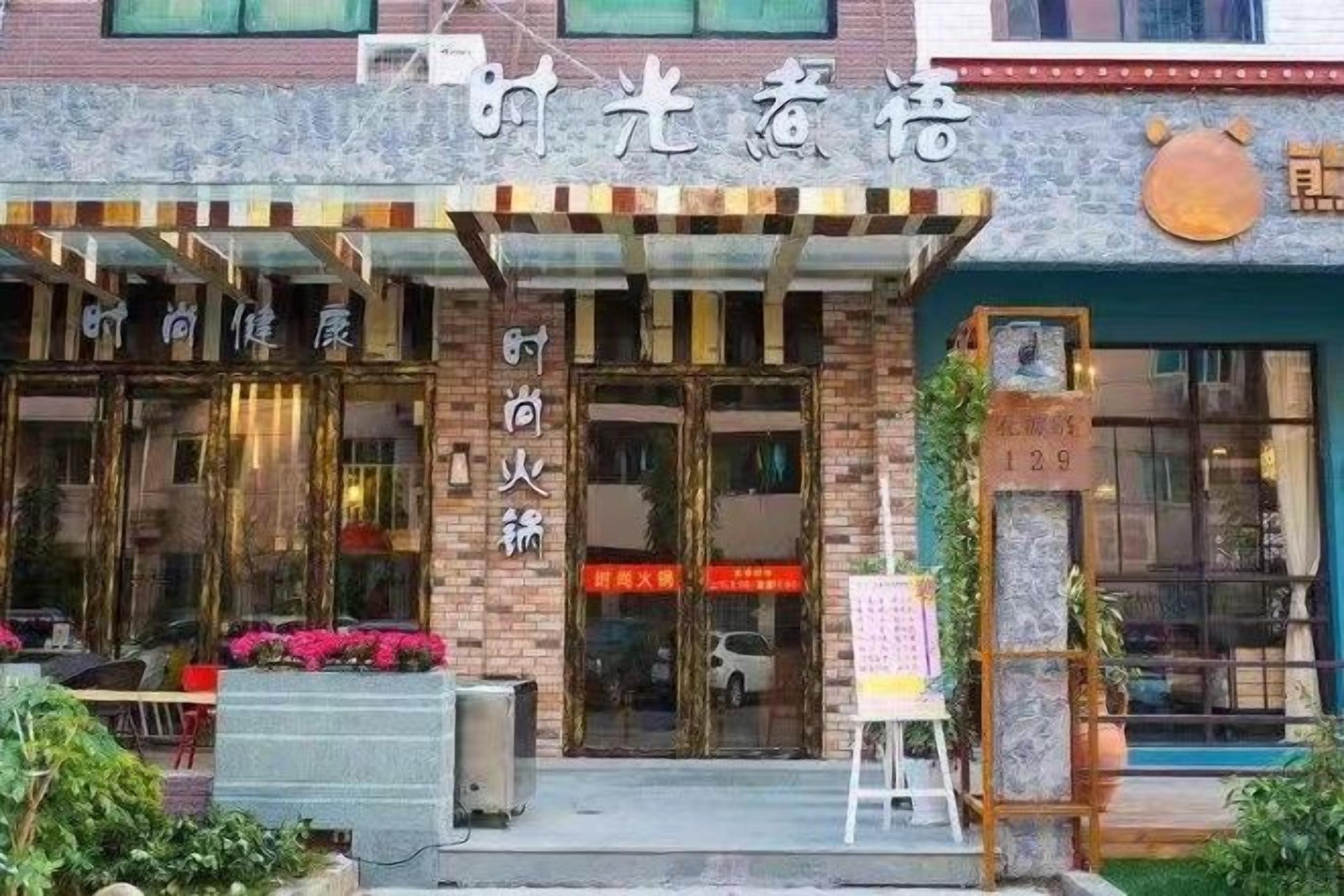 A building with a sign that reads 'Time Glow Hotel.' There are two visible doors with glass panels, and a small signboard with numbers '129' in front of the entrance.