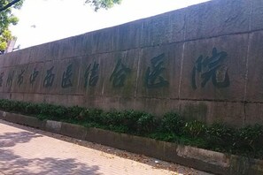 A stone wall with carved text, a paved walkway, and a low hedge.