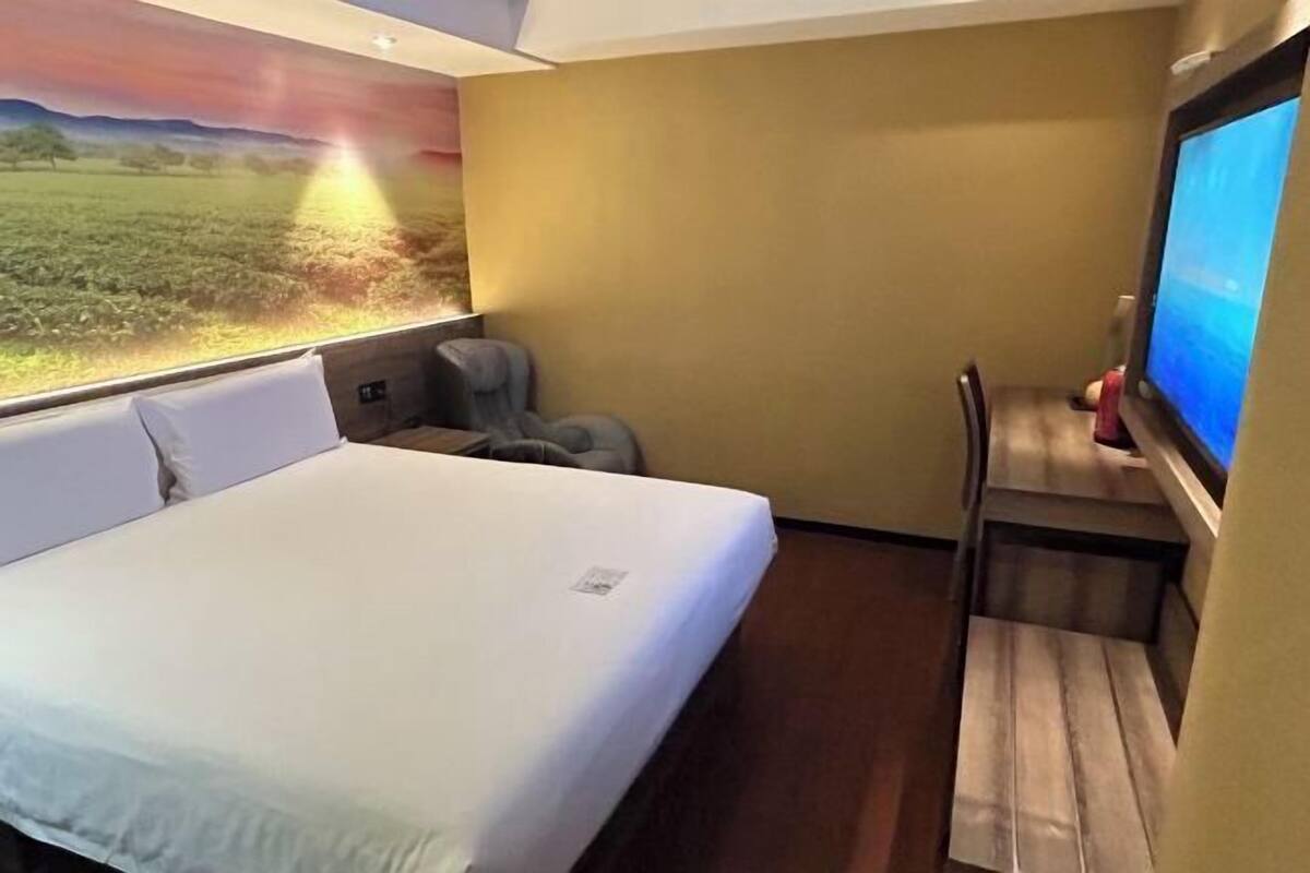 Ein Hotelzimmer mit Bett, Schreibtisch, Stuhl, Fernseher und Wandgemälde.