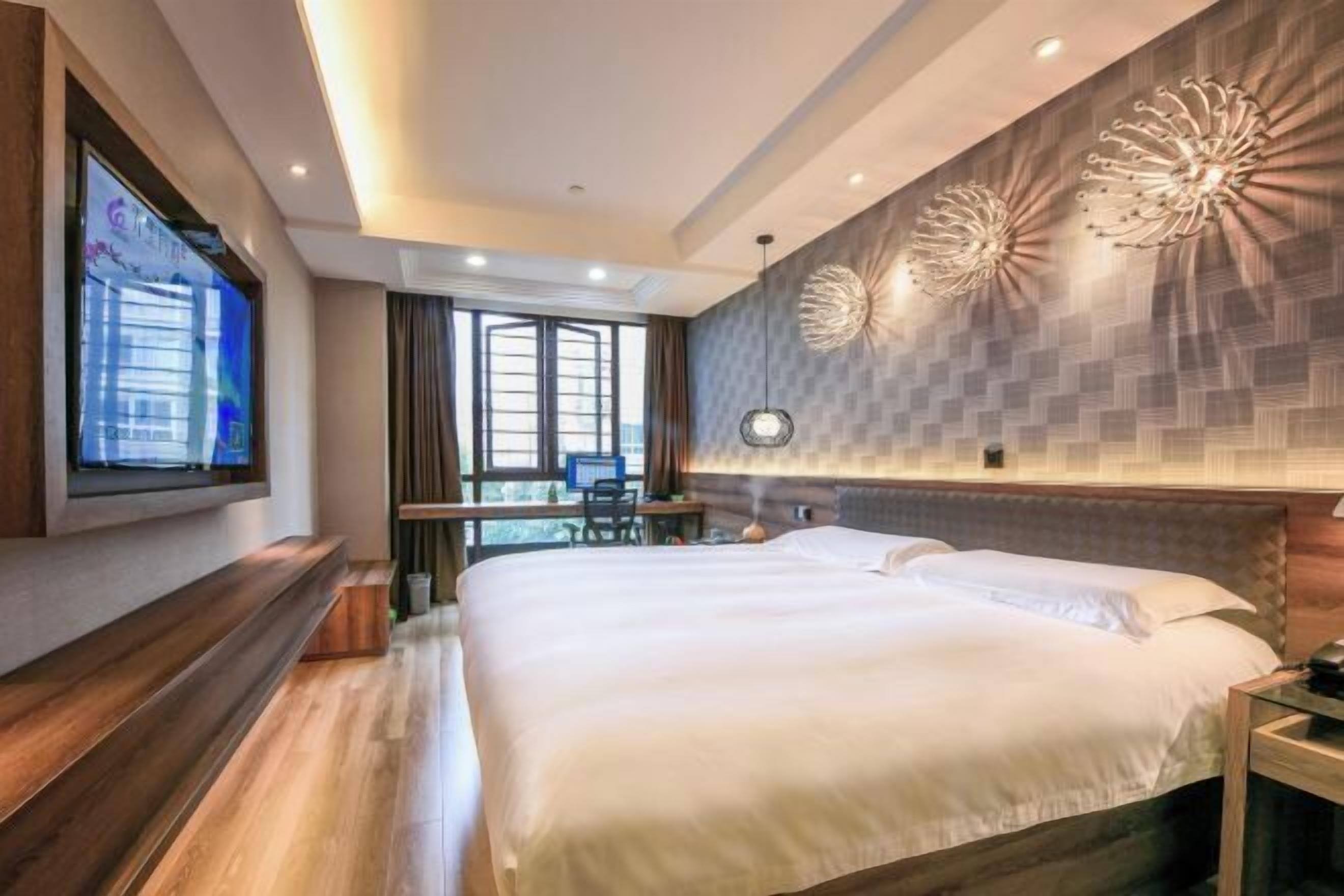 A modern hotel room with a large bed, a desk, and a TV mounted on the wall.