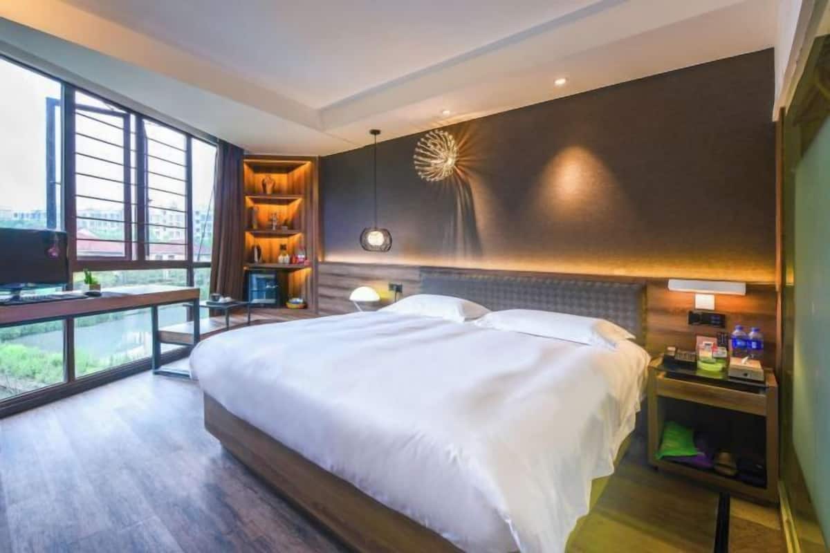 Ein modernes Hotelzimmer mit einem großen Bett, einem Schreibtisch mit Computer, einem Fernseher und einem Balkon mit Stadtblick.