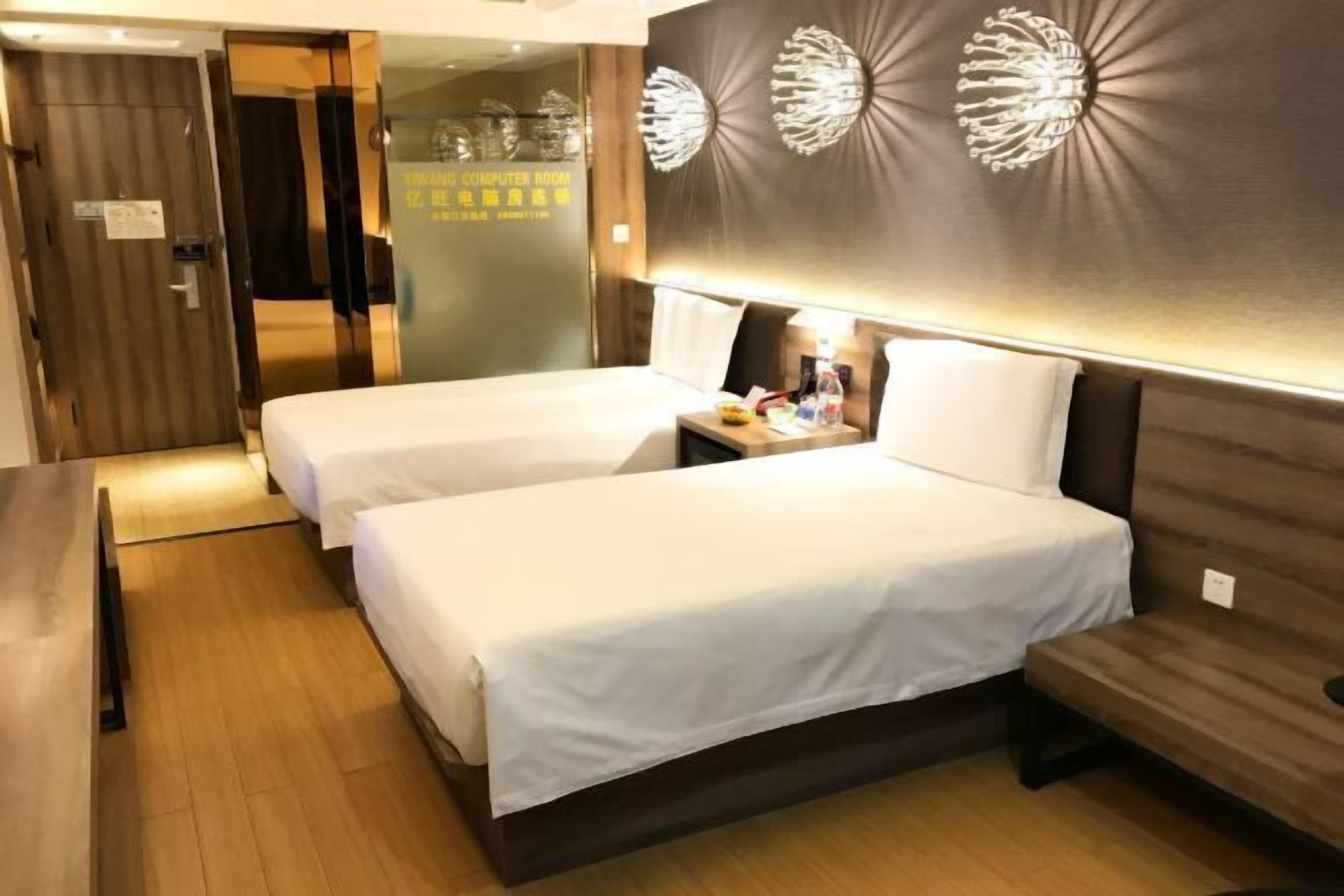A hotel room with two beds, a wooden floor, a desk with a lamp, and a wall with decorative elements.