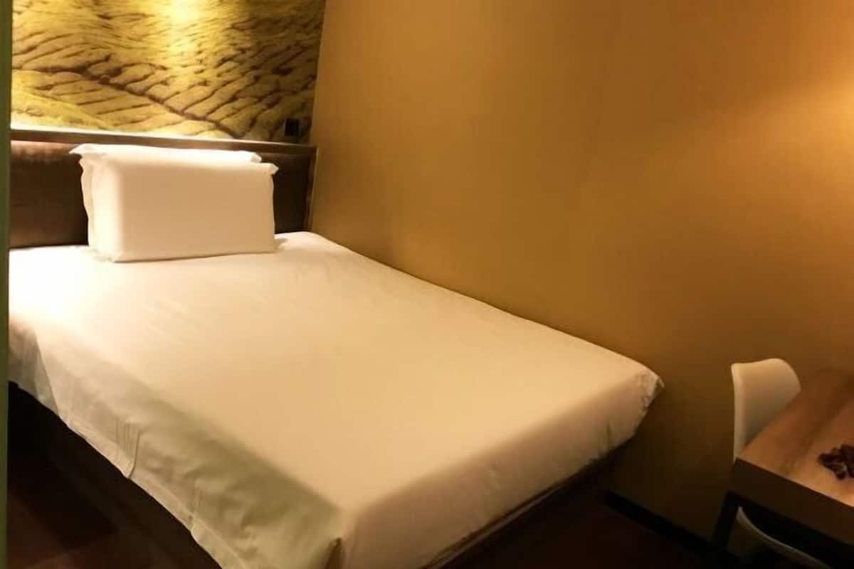 Ein Einzelbett mit weißer Bettwäsche, ein Nachttisch aus Holz, ein Stuhl und eine strukturierte Wand.