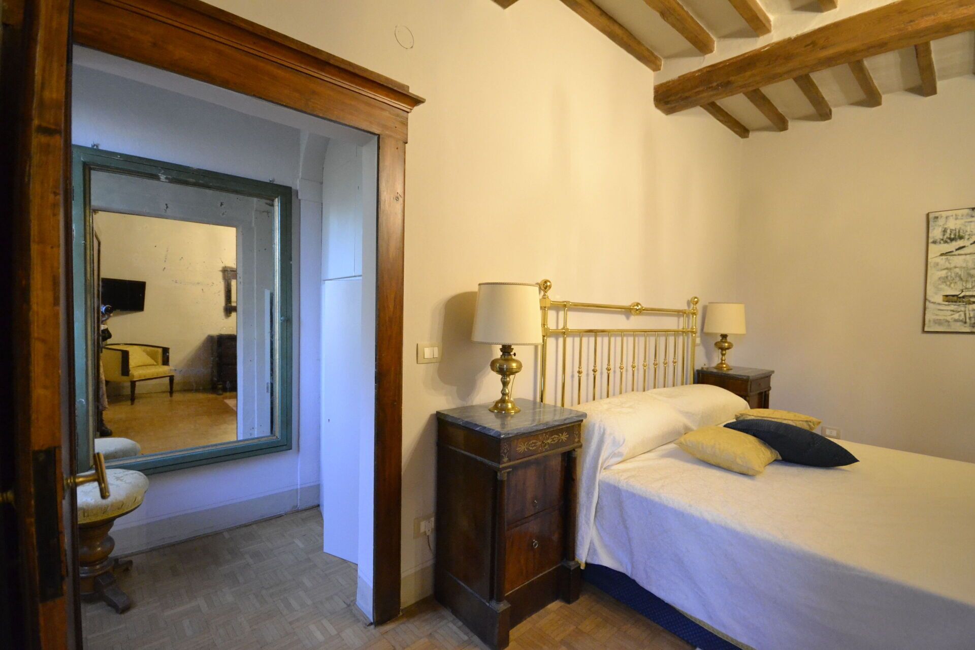Un dormitorio con cama, lámparas de noche, una mesita de noche de madera, un espejo y una silla.