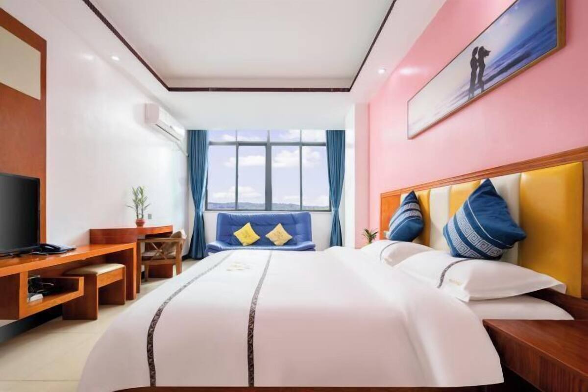 Hotellihuone, jossa on suuri sänky, työpöytä tietokoneella, televisio ja ikkuna, josta avautuu näkymä taivaalle.