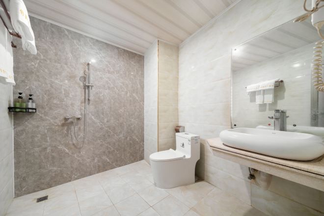 A modern bathroom with a marble shower, a white toilet, and a large sink with a mirror.