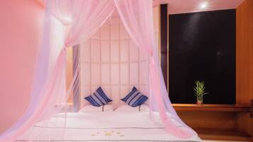 A bedroom with a bed, canopy, pillows, and a small plant.