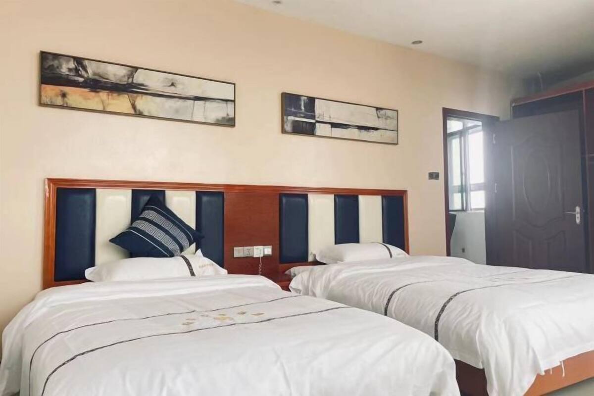 Hotellihuone, jossa on kaksi sänkyä, beigen sävyiset seinät ja kaksi abstraktia maalausta.