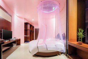 A bedroom with a bed under a canopy, a television on a stand, and a potted plant. - Jindian Business Hotel (Lingao)