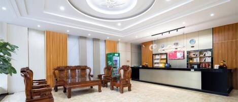 Un vestíbulo de hotel con mostrador de recepción, mobiliario de madera, una máquina expendedora e iluminación empotrada en el techo.