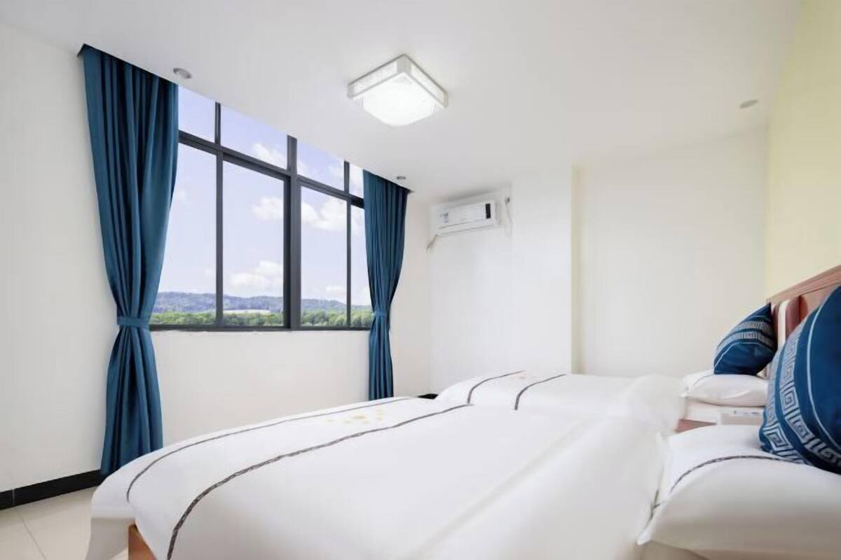 Hotellihuone, jossa on suuri ikkuna, valkoisilla lakanoiden peitetty sänky ja kattovalaisin.
