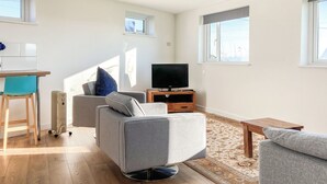 A modern living room with a grey sofa, a wooden coffee table, a TV on a wooden stand, and a small rug.