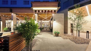 L’entrée d’un hôtel, avec une enseigne indiquant « CAMPEIRE », des places assises à l’extérieur et un espace couvert agrémenté de guirlandes lumineuses.
