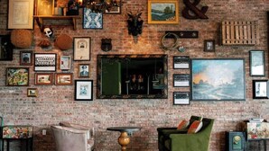 Une pièce chaleureuse avec un mur en briques, divers tableaux encadrés, une cheminée et un fauteuil vert.