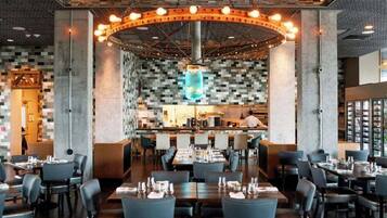A modern restaurant with a central bar area, multiple dining tables, and a unique ceiling design.