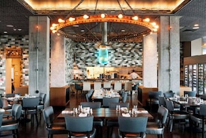 Un restaurante moderno con barra central, varias mesas de comedor y un diseño de techo único.