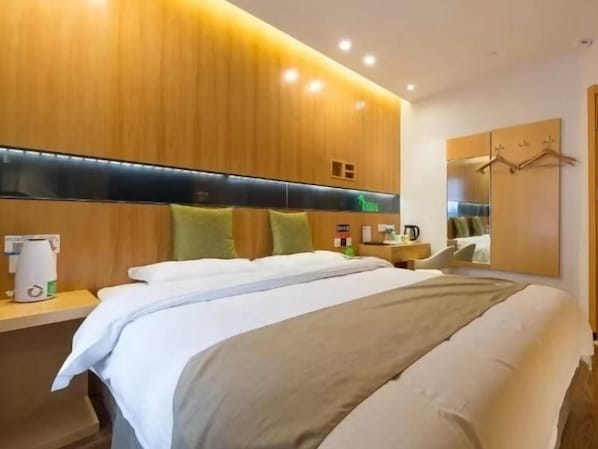 A hotel room with a large bed, wooden headboard, bedside table with a lamp, and a mirror.