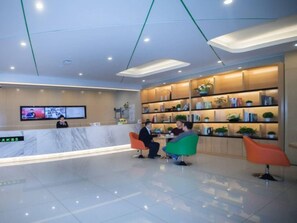 A modern reception area with a marble counter, a television screen, and a seating area with colorful chairs. - Vatica Xuzhou High Speed Railway Station Hotel (Xuzhou)