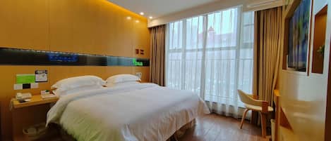 Ein Hotelzimmer mit einem großen Bett, einem Schreibtisch mit Stuhl, einem Fenster mit Vorhängen und einer Klimaanlage.