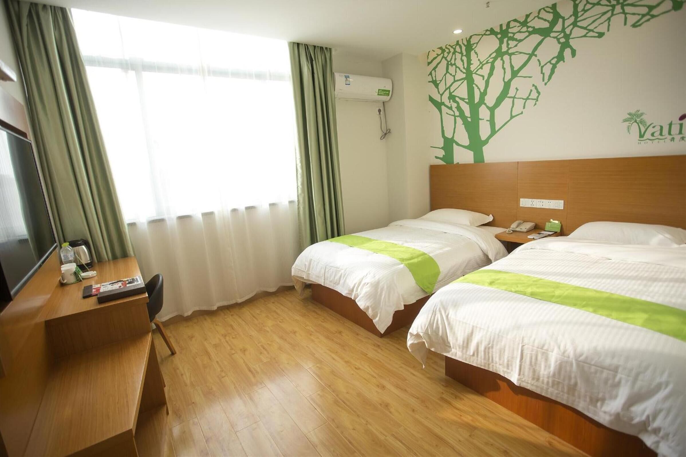 A hotel room with two beds, a desk with a chair, a TV, and a wall-mounted air conditioner.