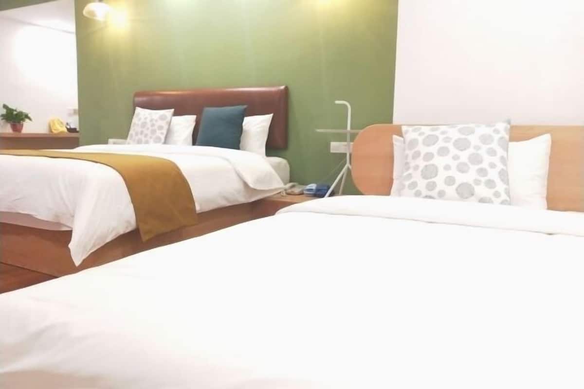A hotel room with two beds, a wooden headboard, a bedside table, and a green wall.