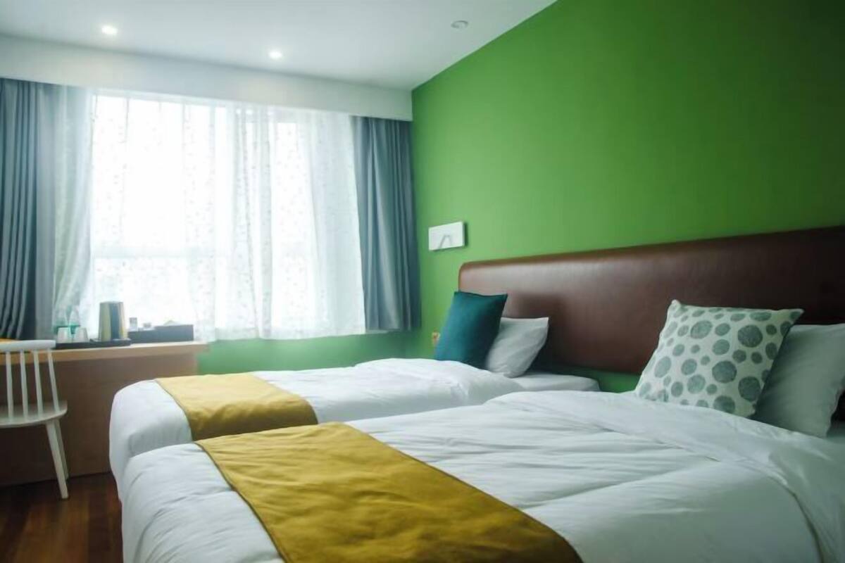 A hotel room with two beds, a desk, and a window with curtains.