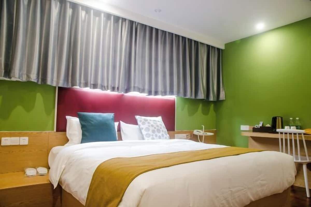 A hotel room with a bed, a desk, a chair, a nightstand, and a window with curtains.