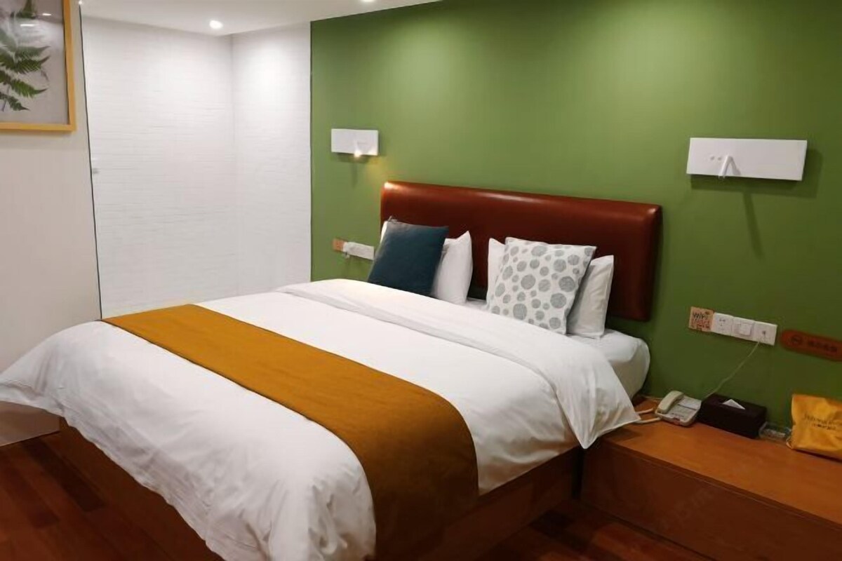 Hotellihuone, jossa on sänky, vihreät seinät, puinen yöpöytä ja valkoinen seinään kiinnitetty puhelin.