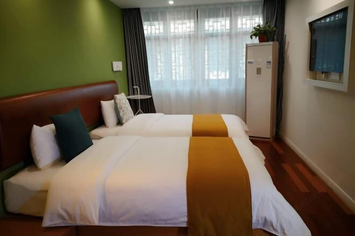 A hotel room with two beds, a small table, a cabinet, and a window with curtains.