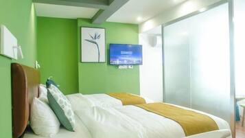 A hotel room with a bed, green walls, a flat-screen TV, and a window.