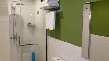 A bathroom with a glass-enclosed shower, white tiled walls, a green accent wall, and a toilet with a white lid.