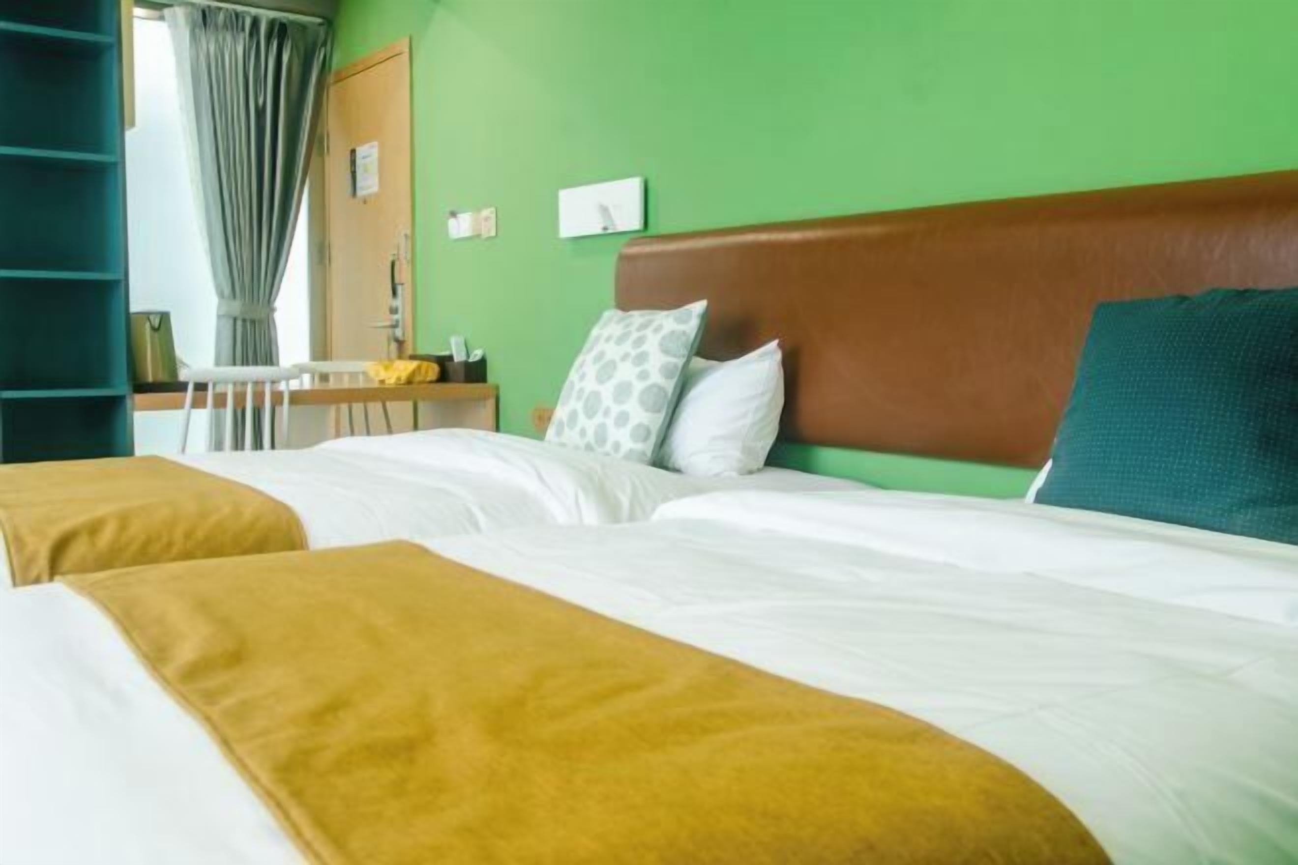 Een hotelkamer met twee bedden, een houten hoofdeinde, een bureau en een stoel.