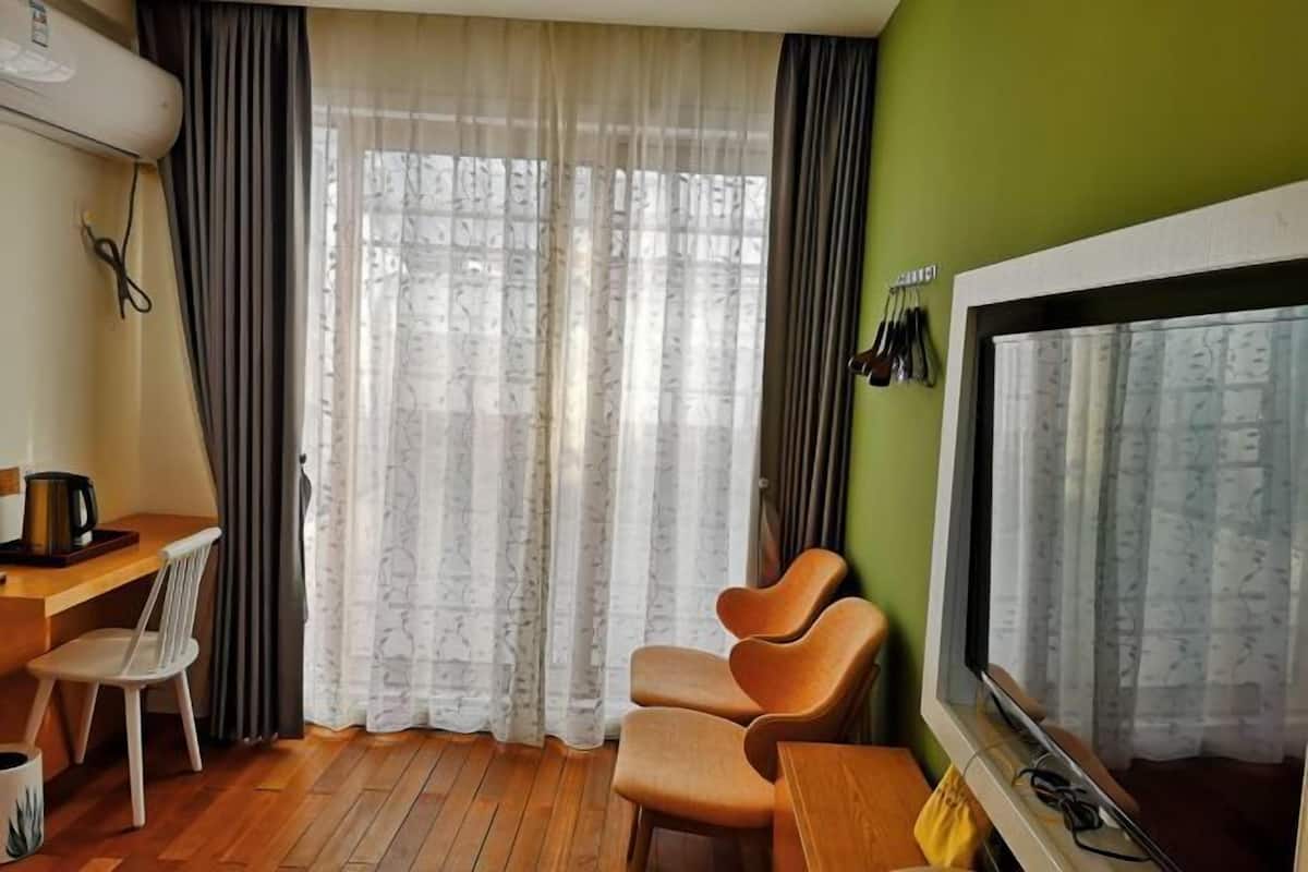 A room with a wooden floor, a desk with a chair, a sofa, a television, and a window with curtains.