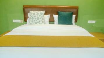 Una cama con cabecera marrón, almohadas blancas y verdes, y una colcha amarilla en una habitación con paredes verdes.