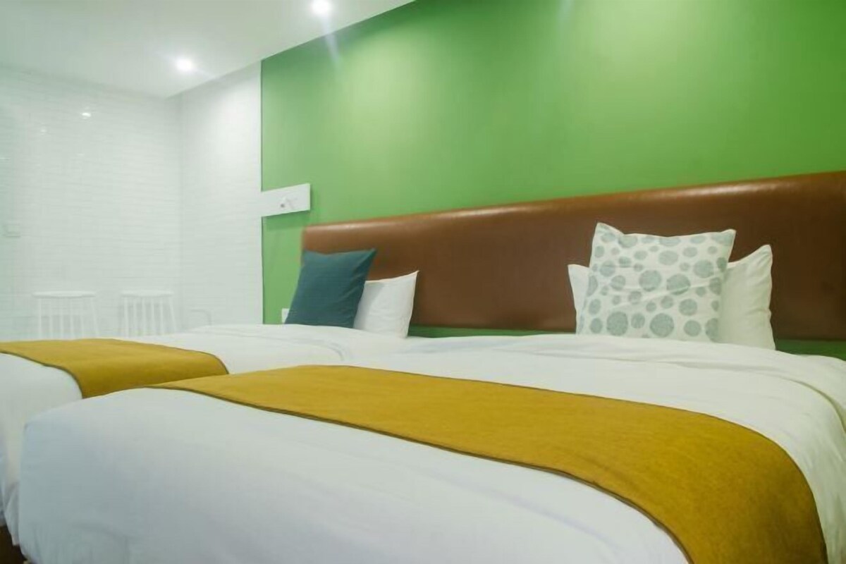 Hotellihuone, jossa on kaksi sänkyä, vihreät seinät, valkoiset vuodevaatteet ja ruskea pääty.